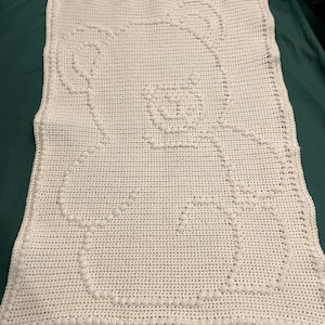 Può includere: Una copertina per neonati in crochet bianco con un motivo a cerchi in rilievo. La copertina è realizzata con un filato morbido e testurizzato.