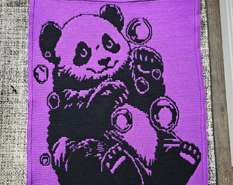 May include: A square, crocheted blanket with a black panda bear design on a purple background. The panda is surrounded by bubbles. The blanket has a solid purple border.