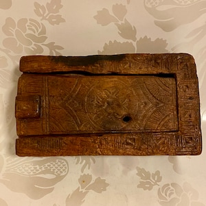 May include: A small, rectangular wooden box with a carved design on the front. The box is made of dark wood and has a hinged lid.