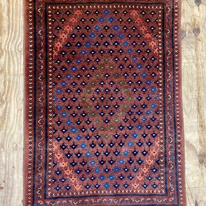 May include: A vintage rug with a geometric pattern in shades of red, blue, and green. The rug has a fringe border and is made of wool.