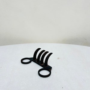 Può includere: Uno strumento in metallo nero a forma di artiglio con due manici circolari. Lo strumento è progettato per afferrare e tenere oggetti.