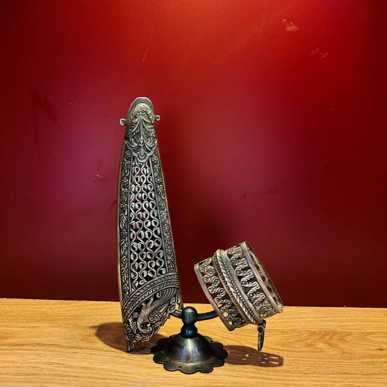 May include: Two silver filigree bracelets on a stand. The bracelets are intricately designed with floral patterns and are made of a silver metal.