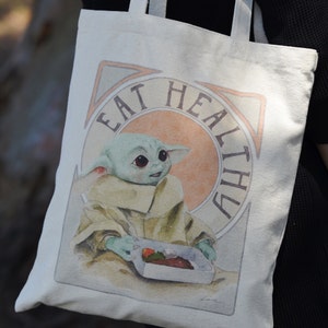May include: A white canvas tote bag with a green character holding a container of food. The bag has the text "Eat Healthy" printed on it.