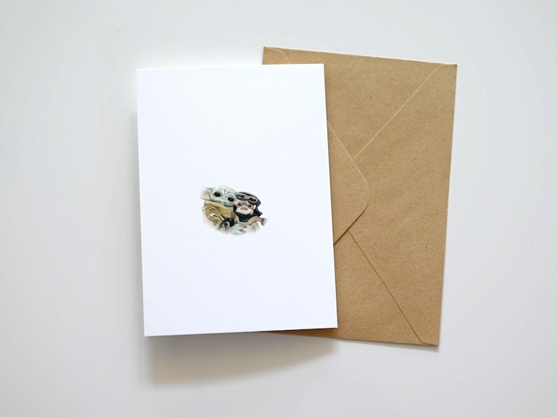 May include: A white greeting card with a small illustration of two characters, and a brown envelope. The card is blank, with the illustration in the center. The envelope is made of brown paper.