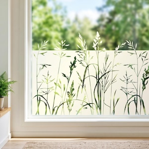 Op de afbeelding: Een rechthoekige raamfolie met een semi-transparante matte afwerking en een gedetailleerde botanische print van hoge groene grassen en weideplanten. Het ontwerp bedekt het onderste deel van het glas en fungeert als een privacy scherm.