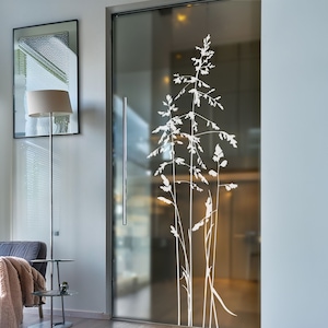 Könnte beinhalten: Eine Milchglastür mit einer weißen Silhouette von hohem Gras. Die Tür befindet sich in einem modernen Haus mit einer grauen Wand und einer Stehlampe.