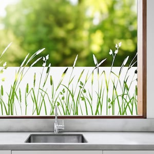 K&ouml;nnte beinhalten: Wei&szlig;e, gefrostete Fensterfolie mit einer gr&uuml;nen Silhouette von hohem Gras und Wildblumen. Die Folie ist an einem Fenster in einer K&uuml;che mit einem Sp&uuml;lbecken aus Edelstahl angebracht.