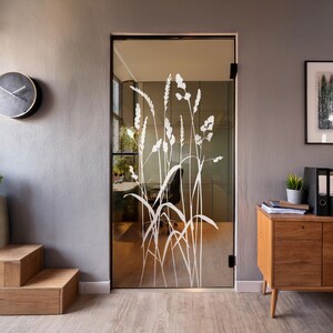 Puede incluir: Una puerta de vidrio esmerilado con una silueta blanca de hierba alta y flores. La puerta está en una oficina moderna con un escritorio de madera y una silla.