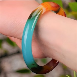 Può includere: Un braccialetto di giada color turchese, verde e arancio. Il braccialetto è realizzato in giada liscia e lucida e presenta un motivo a sfumatura di colore.