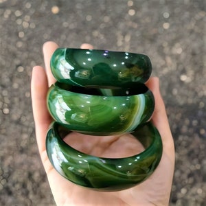 Könnte beinhalten: Drei grüne Achat-Armbänder mit weißen Wirbeln, übereinander gestapelt.