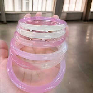 May include: A stack of five pink and white agate bangle bracelets. The bracelets are made of smooth, polished stone and have a natural, organic look.