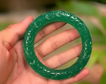 May include: A green jade bangle bracelet with intricate carved designs. The bracelet is smooth and polished.