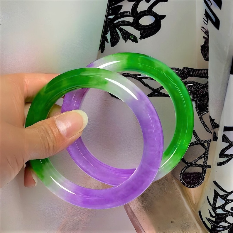 May include: Two jade bangles, one green and one purple, with a white center. The bangles are stacked on top of each other.