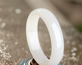 May include: A white jade bangle bracelet, polished to a smooth finish, displayed on a blue and brown stand.