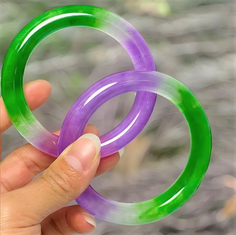May include: Two jade bangles, one green and white, the other purple and white.
