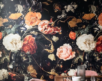 Può includere: Una carta da parati floreale scura con una natura morta di fiori nei toni del bianco, arancione, rosso e rosa. La stanza comprende un tavolo in legno, sedie rosa e vetreria, creando un'elegante sala da pranzo.
