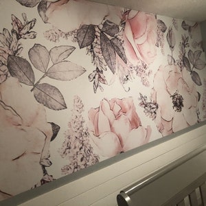 Op de afbeelding: Een witte muur met een bloemenbehang met roze en grijze rozen en bladeren.
