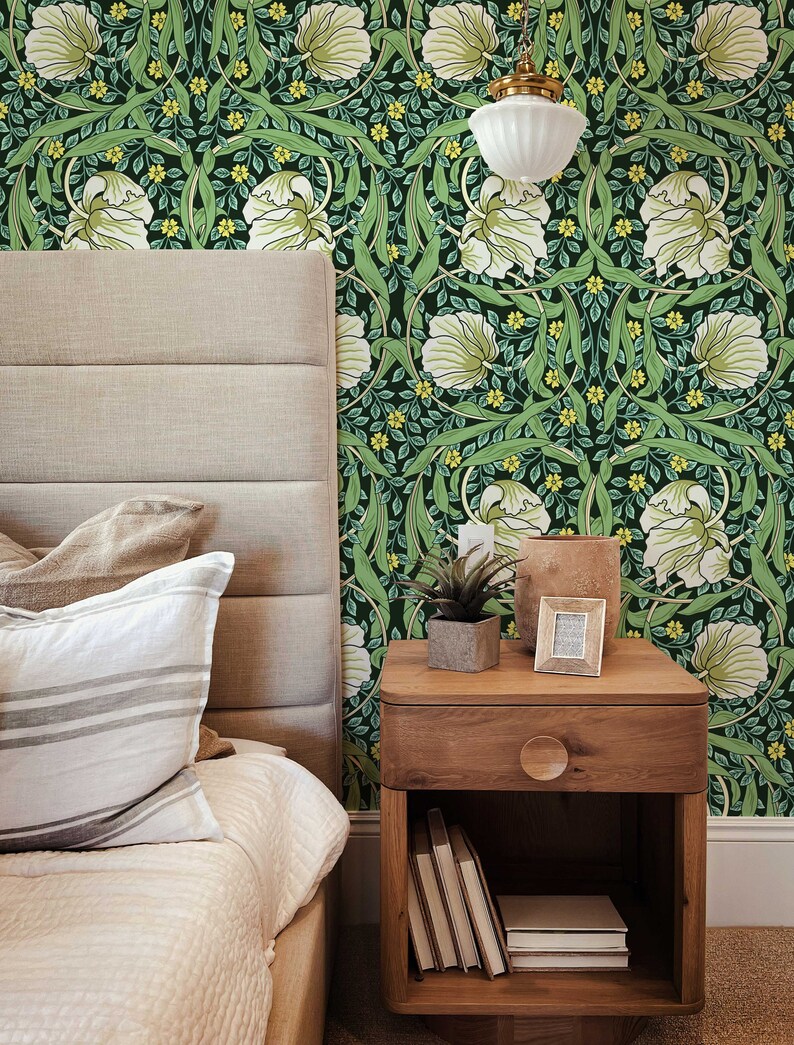 May include: A bedroom with a bed, a nightstand, and a green floral wallpaper. The nightstand has a drawer, a shelf, and a small plant on top. The bed has a white comforter and two pillows.