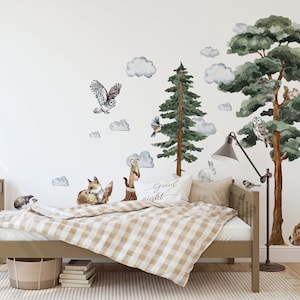 May include: A child's bed with a brown wooden frame and a white and brown checkered comforter. The wall behind the bed is decorated with watercolor animal stickers, including an owl, a fox, a squirrel, a deer, and a lynx. The stickers also include clouds and trees. The text "Good Night" is written on a pillow on the bed.
