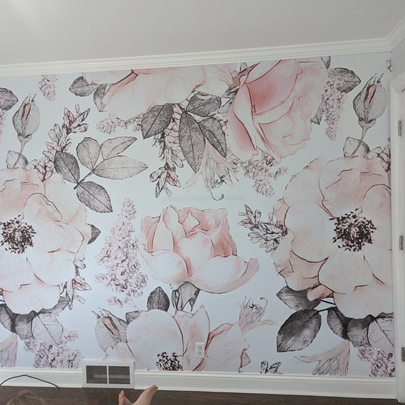 Op de afbeelding: Een witte muur met een bloemenbehang met roze en grijze rozen en bladeren. Het behang heeft een vintage stijl, die doet denken aan aquarel.