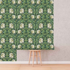 May include: A green and white floral wallpaper pattern with a repeating design of white flowers and green leaves. The wallpaper is shown on a wall with a wooden stool in front of it.
