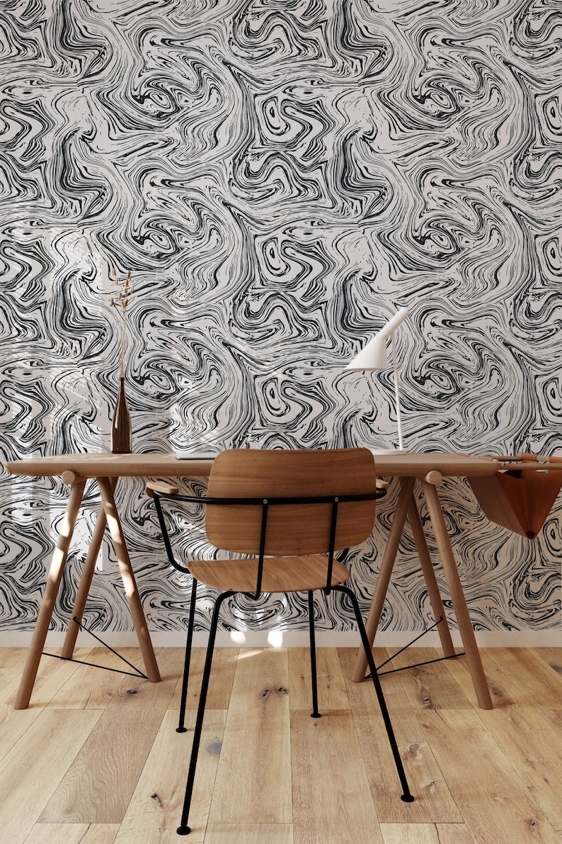 Op de afbeelding: Een houten bureau met een zwarte metalen stoel ervoor. Het bureau heeft een lichte houten afwerking en de stoel heeft een zwart metalen frame en een houten zitting. De muur achter het bureau is bedekt met zwart-wit marmerpapier.