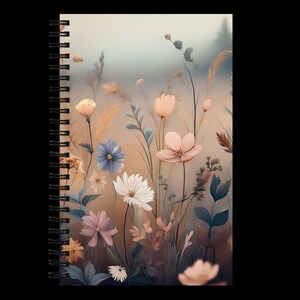 Puede incluir: Cuaderno con espiral con un diseño floral. La portada muestra flores y follaje en colores pastel, incluyendo flores rosas, blancas y azules, sobre un fondo suave y borroso. Tiene una encuadernación en espiral negra, ideal para tomar notas.