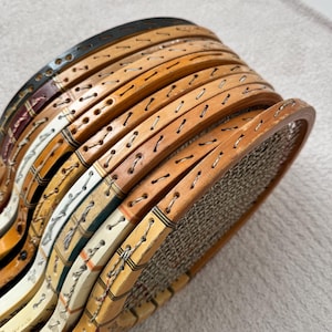 May include: A stack of vintage wooden tennis rackets. The rackets have natural wood tones, with some featuring painted accents in colors like black, white, and burgundy. The strings are visible, and the rackets appear to be in good condition.
