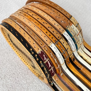 May include: A collection of vintage wooden tennis rackets. The rackets have natural wood frames with visible stringing and decorative accents in black, white, and burgundy. The rackets are stacked, showcasing their unique designs and aged appearance.