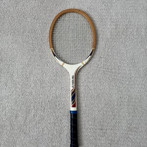 May include: Vintage tennis racket with a wooden frame and a white handle. The racket has the text "JUNIOR PRO" printed on the handle. The grip is black with a blue band. The racket's frame is brown and the strings are silver.