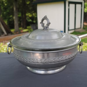 May include: A silver serving bowl with a glass lid and two handles. The bowl has an ornate design and a knob on the lid.