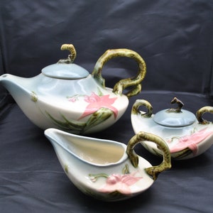 May include: A vintage ceramic tea set with a blue and white floral design. The teapot, creamer, and sugar bowl have green handles and floral accents.