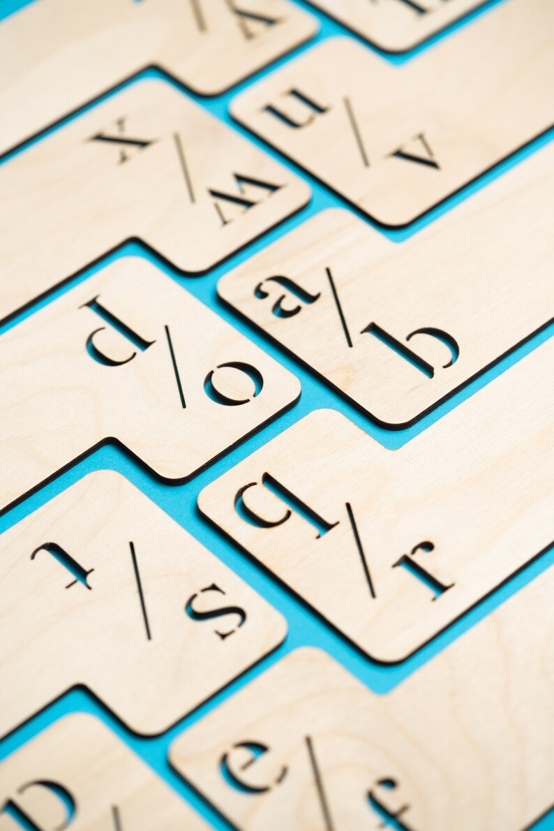 Puede incluir: Azulejos de madera con letras y s&iacute;mbolos sobre un fondo azul. Los azulejos est&aacute;n dispuestos en una cuadr&iacute;cula, con cada azulejo que contiene una sola letra o s&iacute;mbolo. Las letras est&aacute;n en una fuente simple, sin serif.