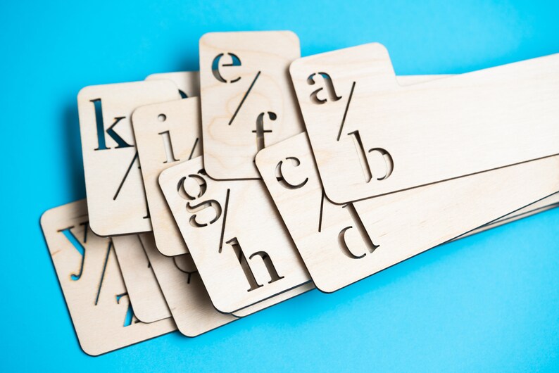 Puede incluir: Un conjunto de plantillas de letras del alfabeto de madera, con letras como "a", "b", "c", "d", "e", "f", "g", "h", "i", "k", "l" e "y" recortadas. Las plantillas est&aacute;n apiladas unas sobre otras sobre un fondo azul.