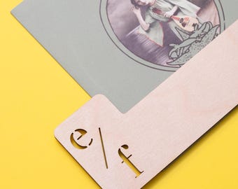 May include: A light-colored wooden bookmark with a notched corner featuring the laser-cut letters e/f. The bookmark is placed over a gray book cover that displays an illustration of a person holding a mandolin inside a circular frame.