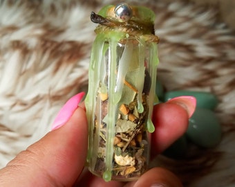 May include: A small glass bottle filled with dried herbs and spices, sealed with green wax and tied with twine. The bottle is held in a hand with pink nail polish.