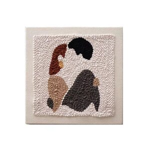 Puede incluir: Un tapiz de pared de lona beige con un dise&ntilde;o cosido a mano de dos figuras abstractas en marr&oacute;n, beige y negro.
