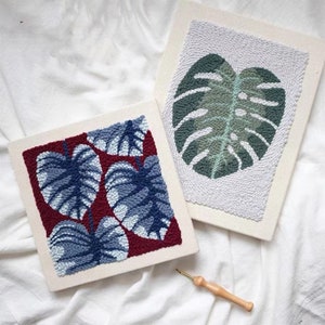 Op de afbeelding: Twee ingelijste stukken naaldkunst met blauwe en groene bladeren op een witte achtergrond. De naaldkunst is uitgevoerd in een ronde steek.
