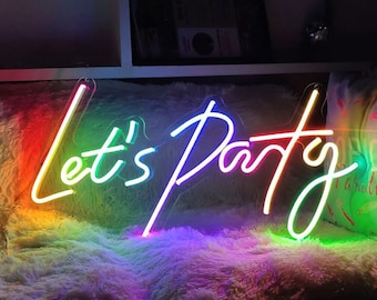 May include: A neon sign with the words "Let's Party" in rainbow colors. The sign is on a white fluffy surface.
