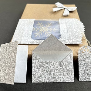 May include: A set of four white envelopes with a gray and white patterned design. The envelopes are all different sizes and are arranged on a brown surface.