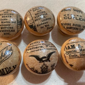 May include: Six vintage wooden knobs with various advertisements printed on them. The advertisements include: "Row Boats and Hunting Boats", "A Full Line of Launch and Engine Fittings Search Lights", "Barbers' Supply Dealer Cutlery", "The Compressed Dustless Method Thurman Patent Company", "Meng & Sh Manufacturers, Wholesale Hatters, Furs Seal and Fur Garments a Specialty", and "Sam A. Long Special Machinery Tools, Dies, Etc."