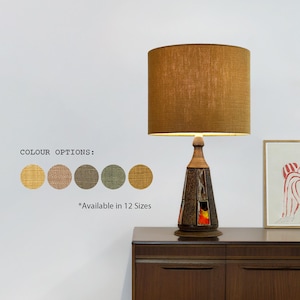 May include: A table lamp featuring a brown lampshade and a distinctive base with a geometric design. The image displays colour options and the text "Available in 12 Sizes". The lamp is a decorative item.