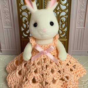 May include: A white rabbit doll wearing a peach crocheted dress with a pink ribbon.