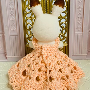 May include: A small, white rabbit wearing a peach-colored crocheted dress with a scalloped hem.