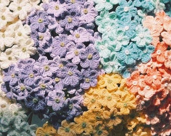 May include: A bouquet of crocheted flowers in various pastel colors, including white, light blue, lavender, peach, and yellow.