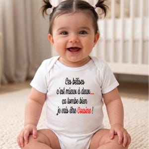 以下が含まれることがあります： 「Les bêtises c'est mieux à deux... ça tombe bien je vais être Cousine!」と黒と赤で書かれた白いベビーボディスーツ。2つの小さなポニーテールをした笑顔の赤ちゃんが着ています。