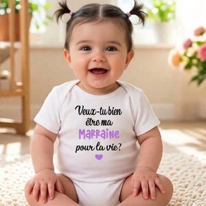 May include: A smiling baby wearing a white onesie with the French text "Veux-tu bien &ecirc;tre ma Marraine pour la vie?" in black and purple, with a purple heart. The baby has dark hair in pigtails.