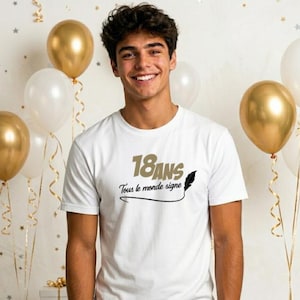 Può includere: T-shirt bianca con la scritta "18 ANS Tous le monde signe" in oro e nero. La maglietta è indossata da una persona che sorride davanti a palloncini dorati e bianchi, suggerendo una festa di compleanno.