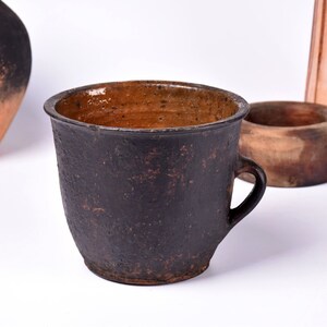 May include: A dark brown ceramic mug with a handle. The mug has a rough, textured surface and a slightly flared rim.