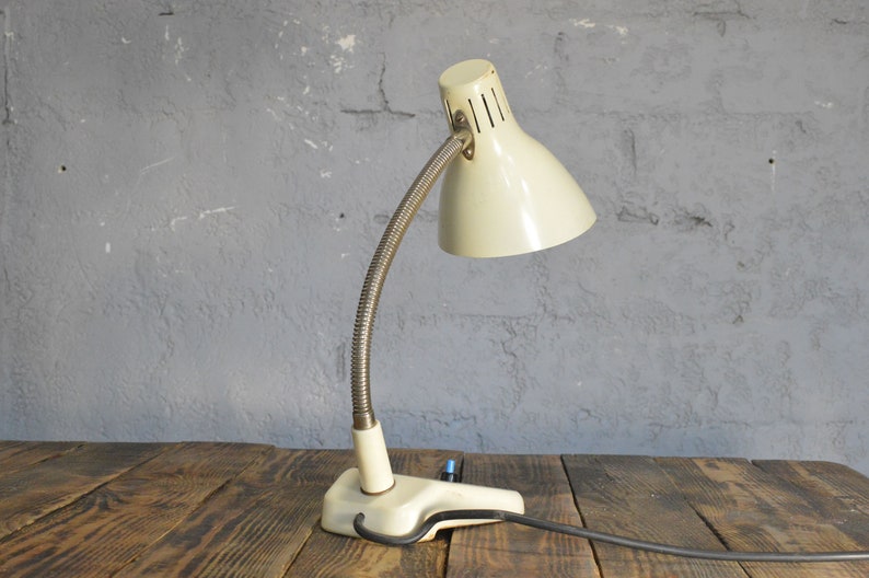 K&ouml;nnte beinhalten: Eine wei&szlig;e Vintage-Tischlampe mit flexiblem Arm und einer Klemmbasis. Die Lampe hat einen wei&szlig;en Metallschirm mit einer silbernen Metallbasis.